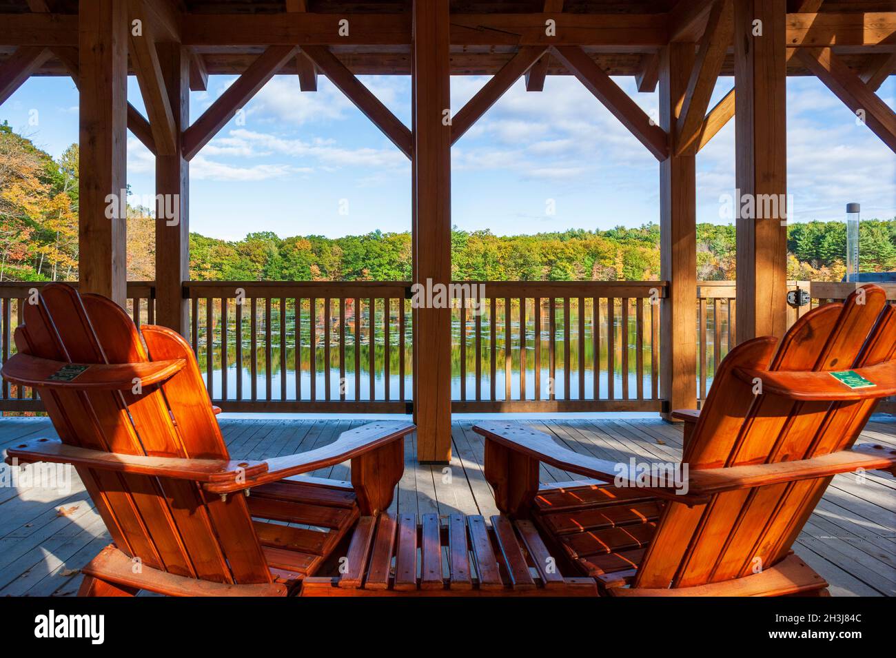 Adirondack Stühle auf dem Deck einer überdachten Fußgängerbrücke mit Blick auf einen See und einen Wald in Herbstfarben. Enchanta Bridge, Moore State Park, Paxton, MA Stockfoto