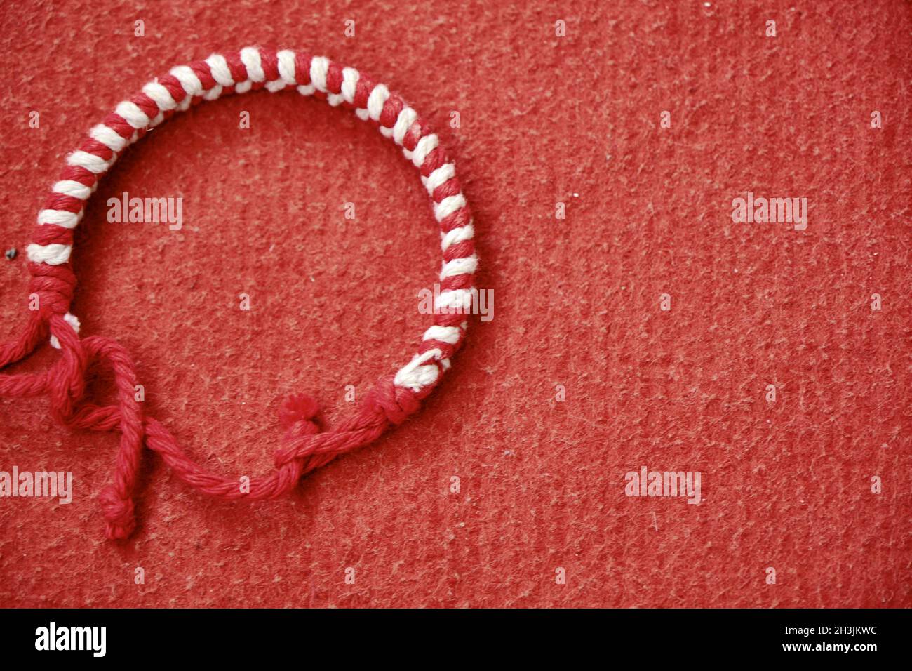 Alte bulgarische Tradition der roten und weißen Farbe Armband martenitsa (baba martha) Armband steht auf der roten Farbe und Stoff Textur Stockfoto