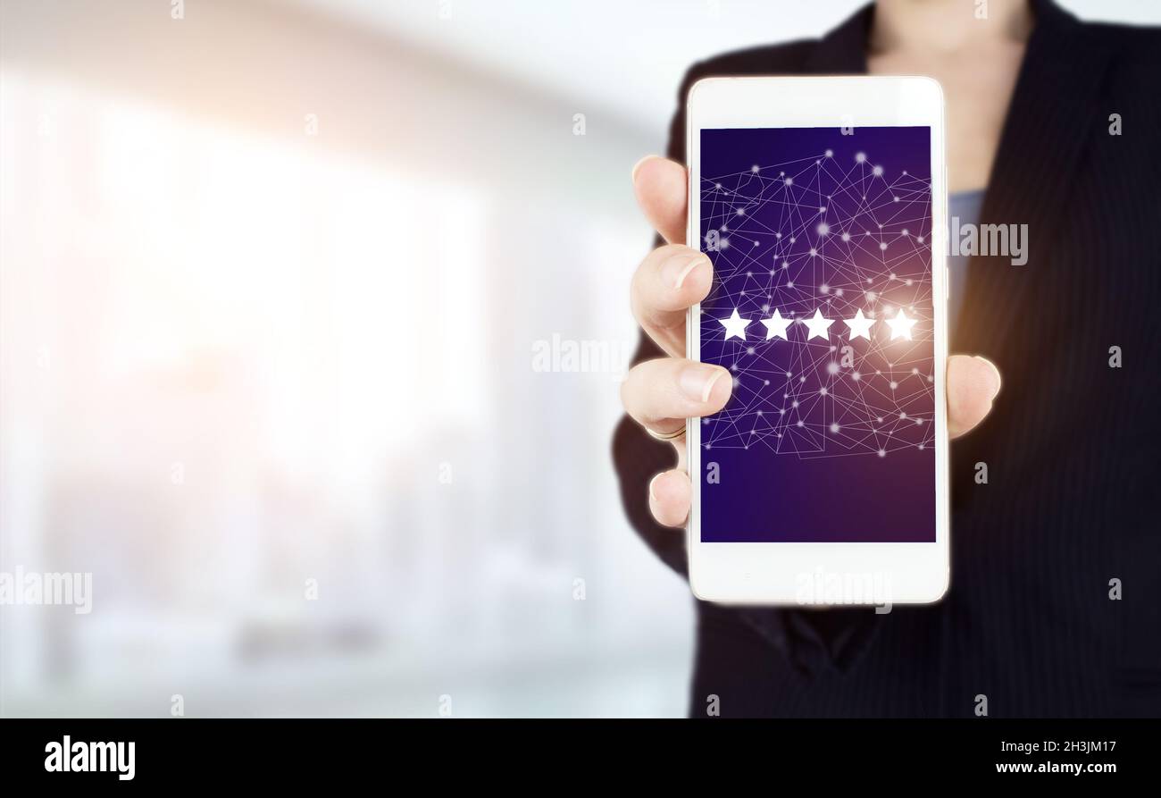 Customer Experience Konzept. Handgriff weißes Smartphone mit digitalem Hologramm fünf Sterne Zeichen auf hellem verschwommenem Hintergrund. Bewertung, Bewertung, Zufriedenheit Stockfoto