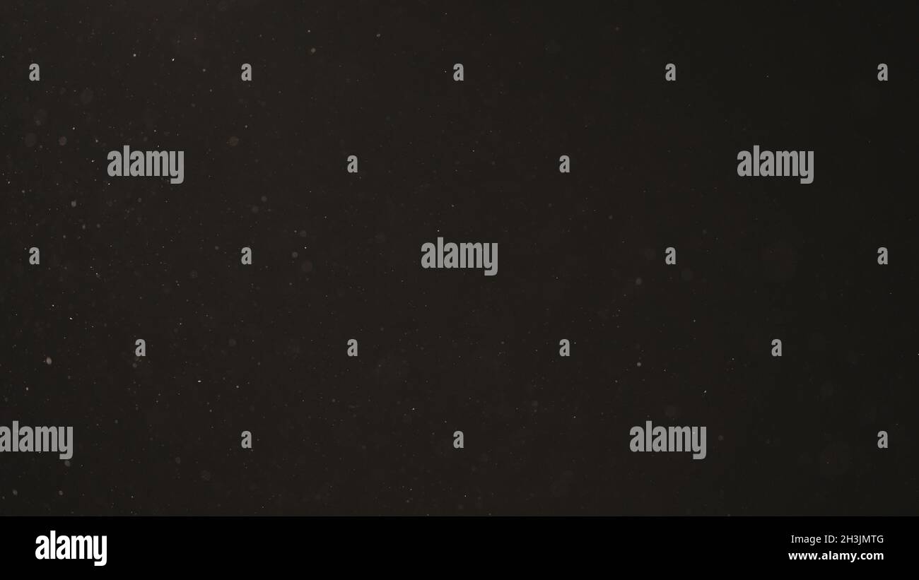 Langsame Staubpartikel schweben in warmem Licht auf schwarzem Hintergrund, 120fps Stockfoto