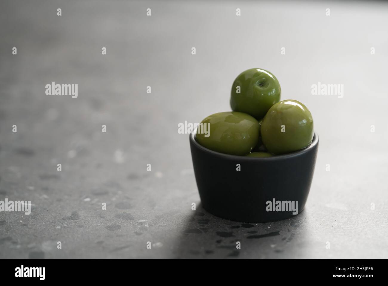 Große grüne Oliven in schwarzer Schale auf Beton Hintergrund, flacher Fokus Stockfoto