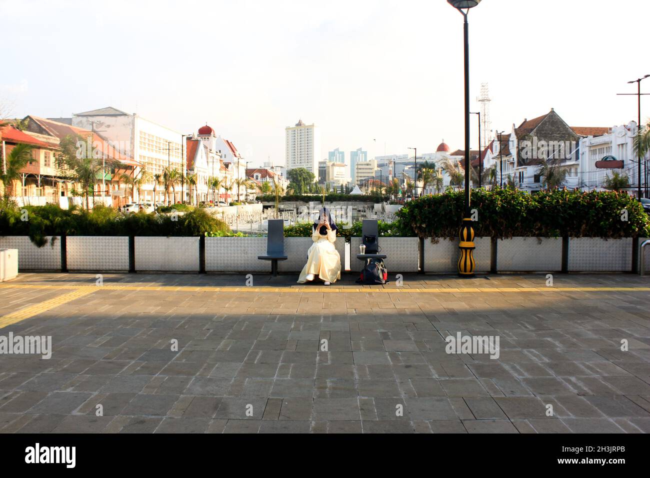 Eine Frau im Hijab-Schleier schaute auf ihr Telefon, während sie auf einer Bank in der Nähe eines Kanals in der Altstadt von Jakarta Kota, Jakarta, Indonesien, saß Stockfoto