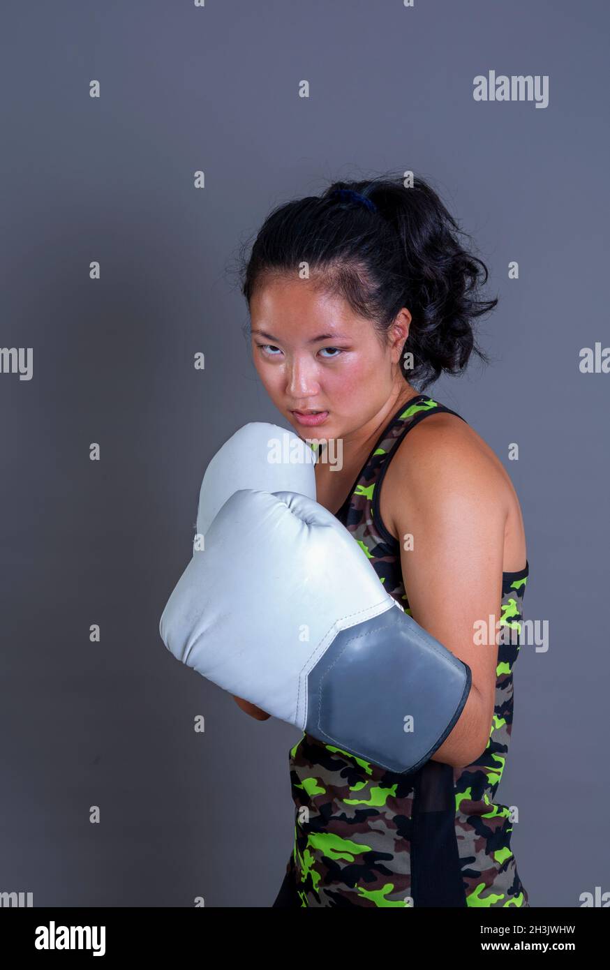 Junge chinesin mit Boxhandschuhen in Wache-Position, die auf die Kamera schaut Stockfoto