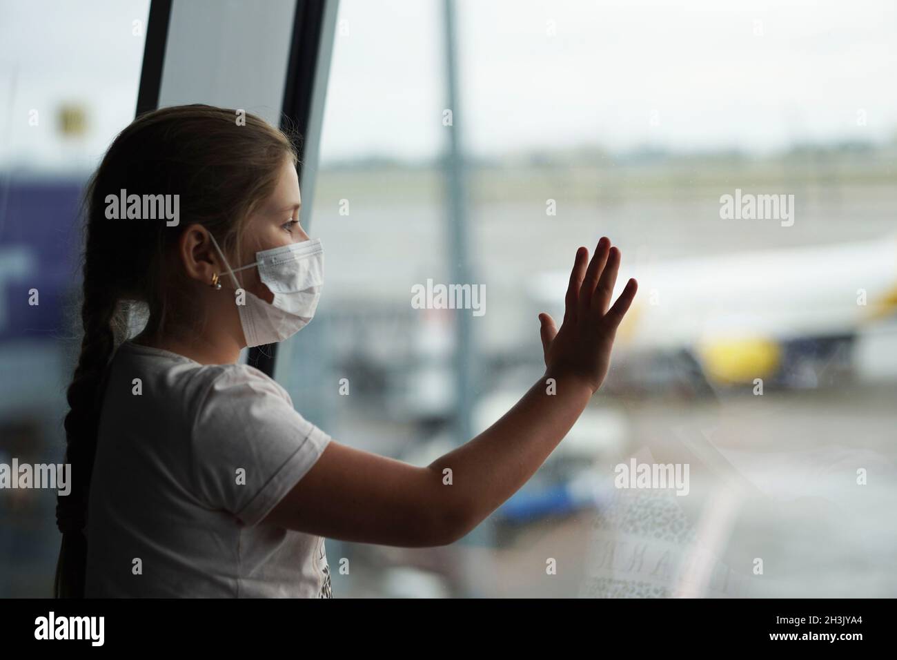 Mädchen mit Gesichtsschutz Maske Blick auf das Fenster zu einem Flugzeug während der Wartezeit am Flughafen. Stockfoto