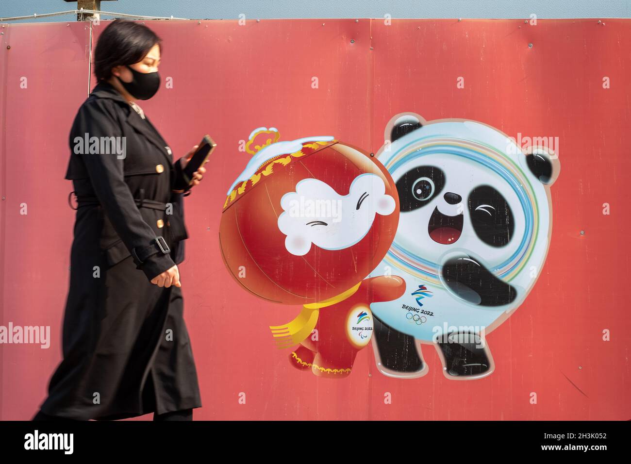 Chinesische Dame geht an einer Plakatwand vorbei, auf der offizielle Maskottchen der Olympischen Winterspiele 2022 in Peking, China, zu sehen sind. 29-Okt-2021 Stockfoto