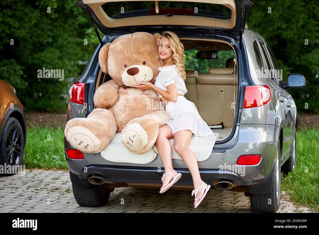 Eine junge Frau umarmt einen riesigen Teddybären im Auto. Stockfoto