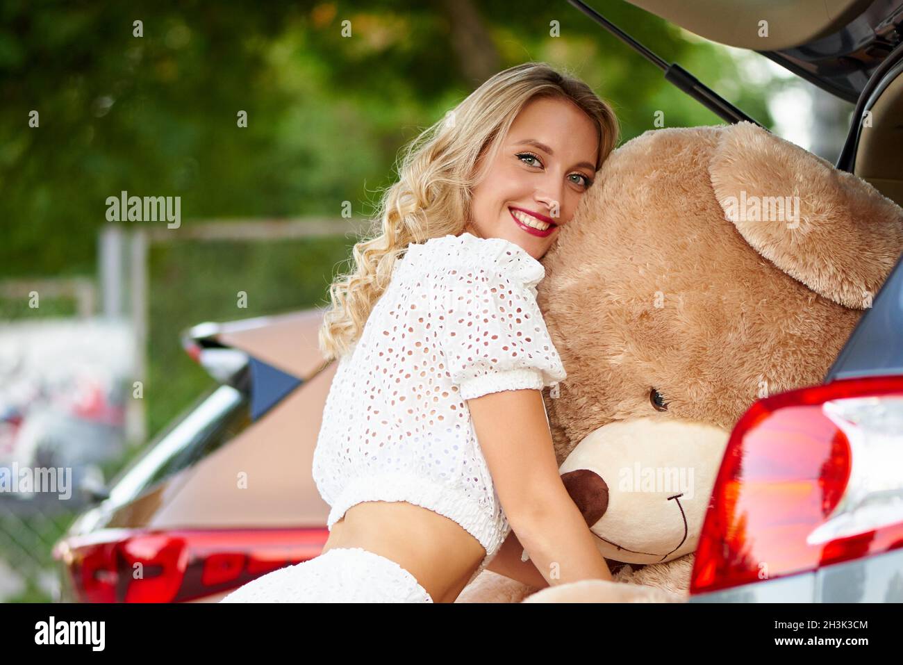 Eine fröhliche junge Frau umarmt einen Teddybären im Auto. Stockfoto