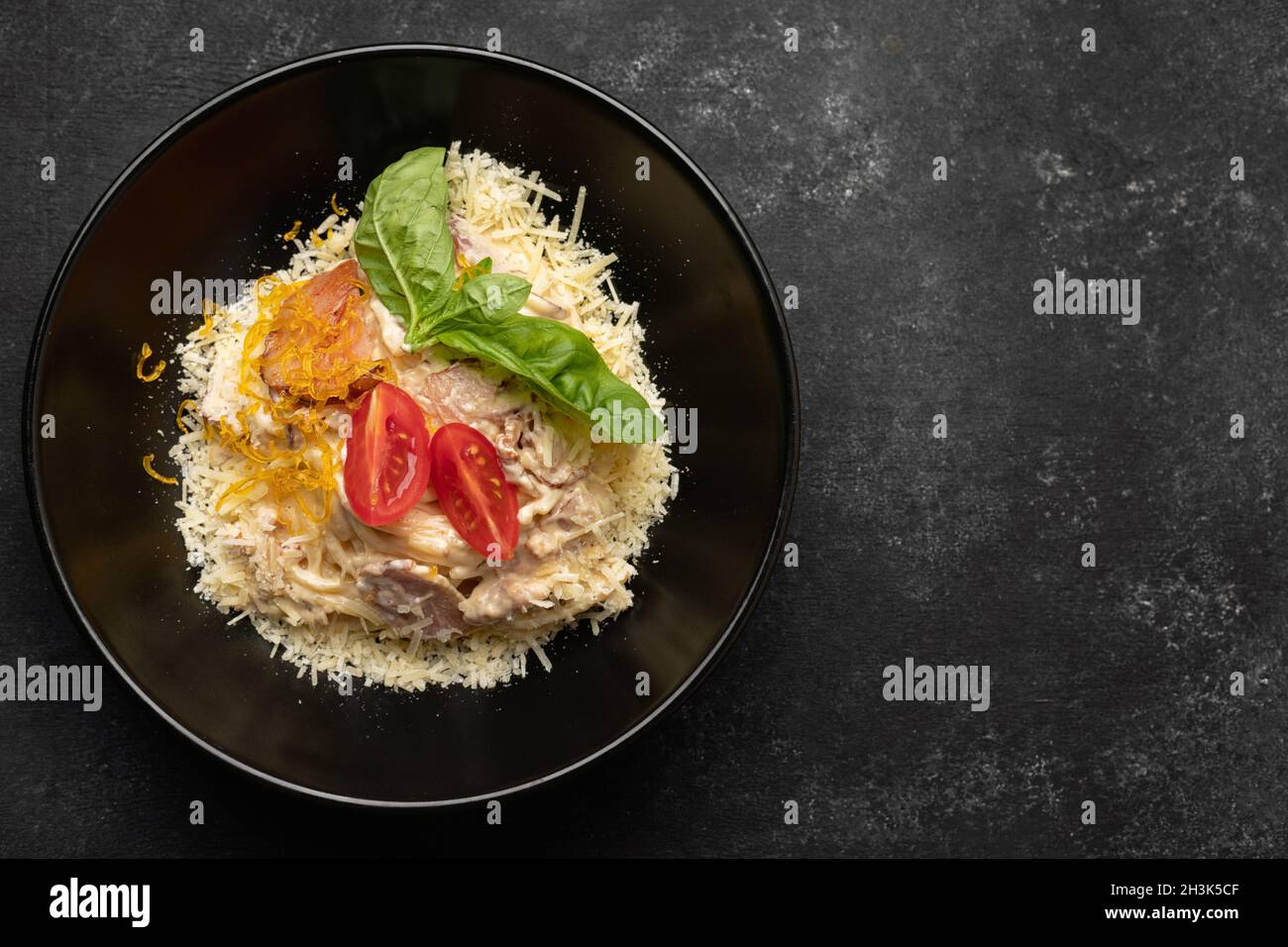 Pasta mit Fleischkäse und Basilikum auf einem schwarzen Teller Stockfoto