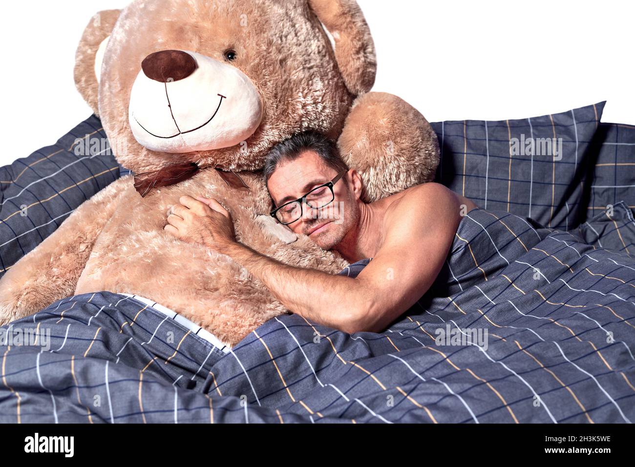 Ein junger Mann schläft in einer Umarmung mit einem Teddybär im Bett. Stockfoto