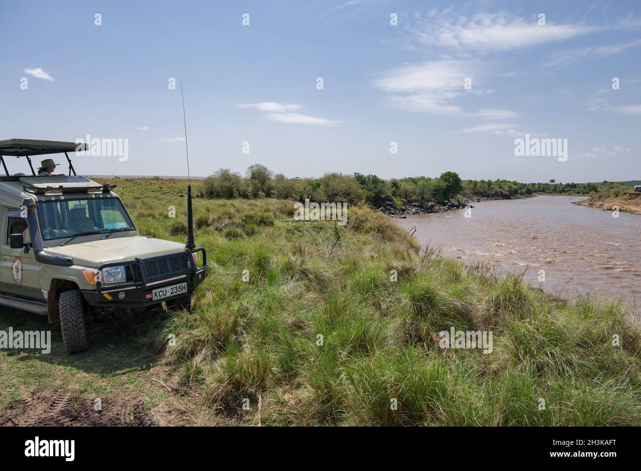 Ein 4x4 Toyota Landcruiser Safari-Fahrzeug mit Touristen, die am Mara Fluss auf Tiere warten, die überqueren, Masai Mara, Kenia Stockfoto