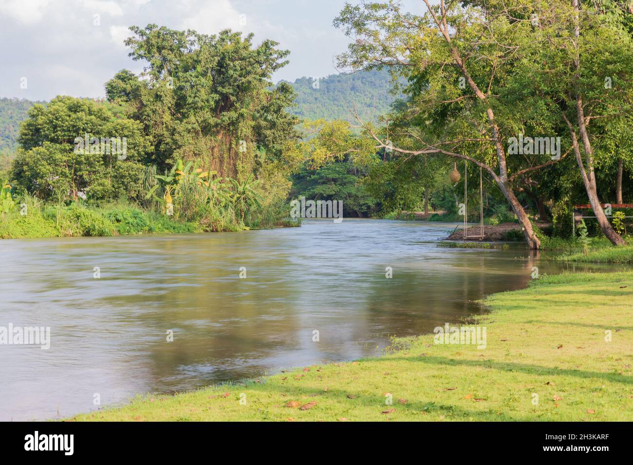 Seilschaukel hängend von einem Baum über einem fließenden Fluss in einer Naturparkumgebung in Thailand mit üppigem grünem Laub und morgendlichen Herbstblättern. Stockfoto