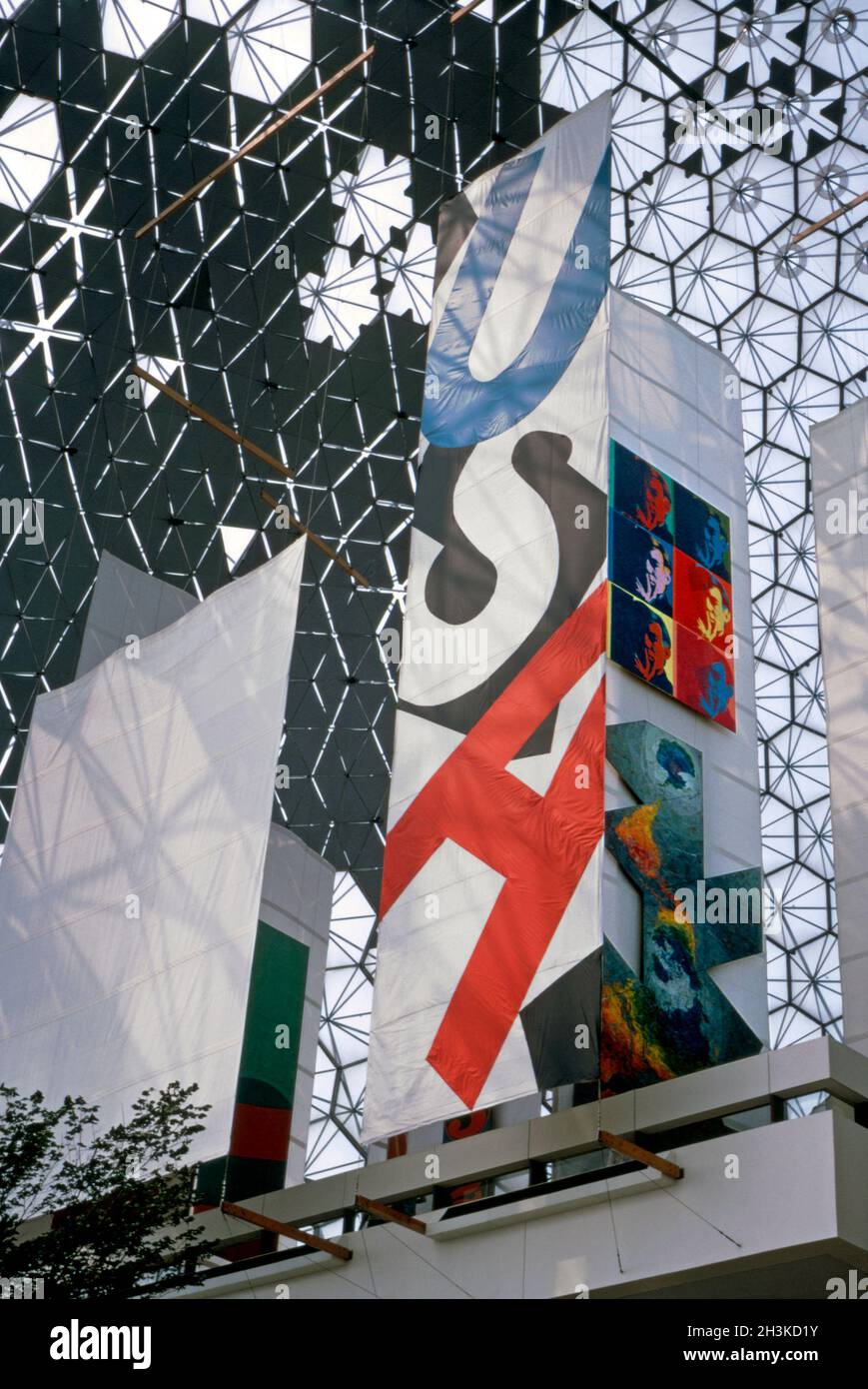 Im Inneren des amerikanischen Pavillons auf der Expo 67, Montreal, Quebec, Kanada im Jahr 1967. Auf einem vertikalen Banner mit den Buchstaben USA sind auch zwei Kunstwerke zu sehen – (Mitte rechts) sechs riesige Selbstporträts des Pop-Künstlers Andy Warhol, darunter Jasper Johns’ ‘Dymaxion Map’. Der Pavillon der USA war eine geodätische Kuppel, die vom Architekten Richard Buckminster Fuller entworfen wurde. Die Attraktion lebte nach 1967 während der Sommermonate weiter und schloss schließlich 1981. Der Pavillon der USA ist heute das Biosphere, ein Museum, das der Umwelt gewidmet ist. Dieses Bild stammt aus einer alten Amateur-Farbtransparenz – einem Vintage-Foto aus den 1960er Jahren. Stockfoto