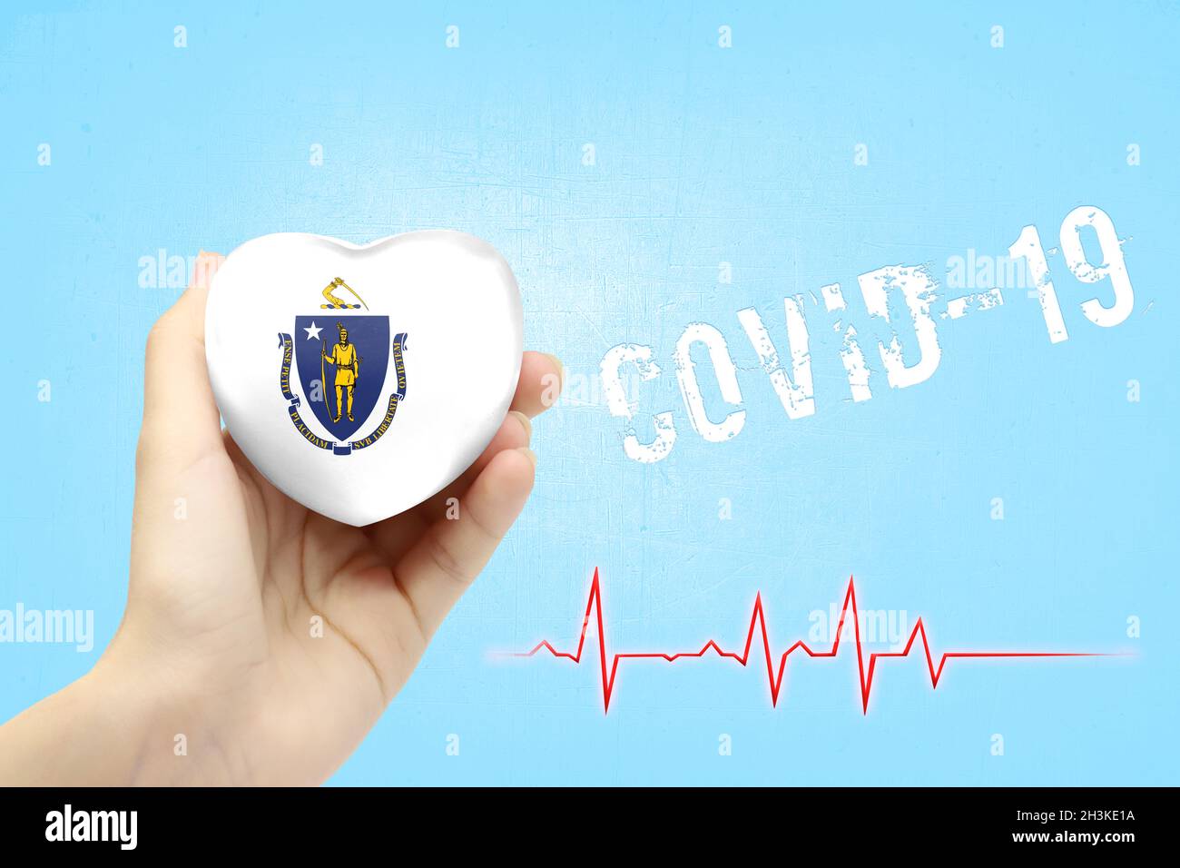 Ein Mädchen hält ein Spielzeug in Form eines Herzens mit der Flagge des Staates Massachusetts, einem Konzept der Gesundheitsversorgung während des Covid-19-Coronavirus pand Stockfoto