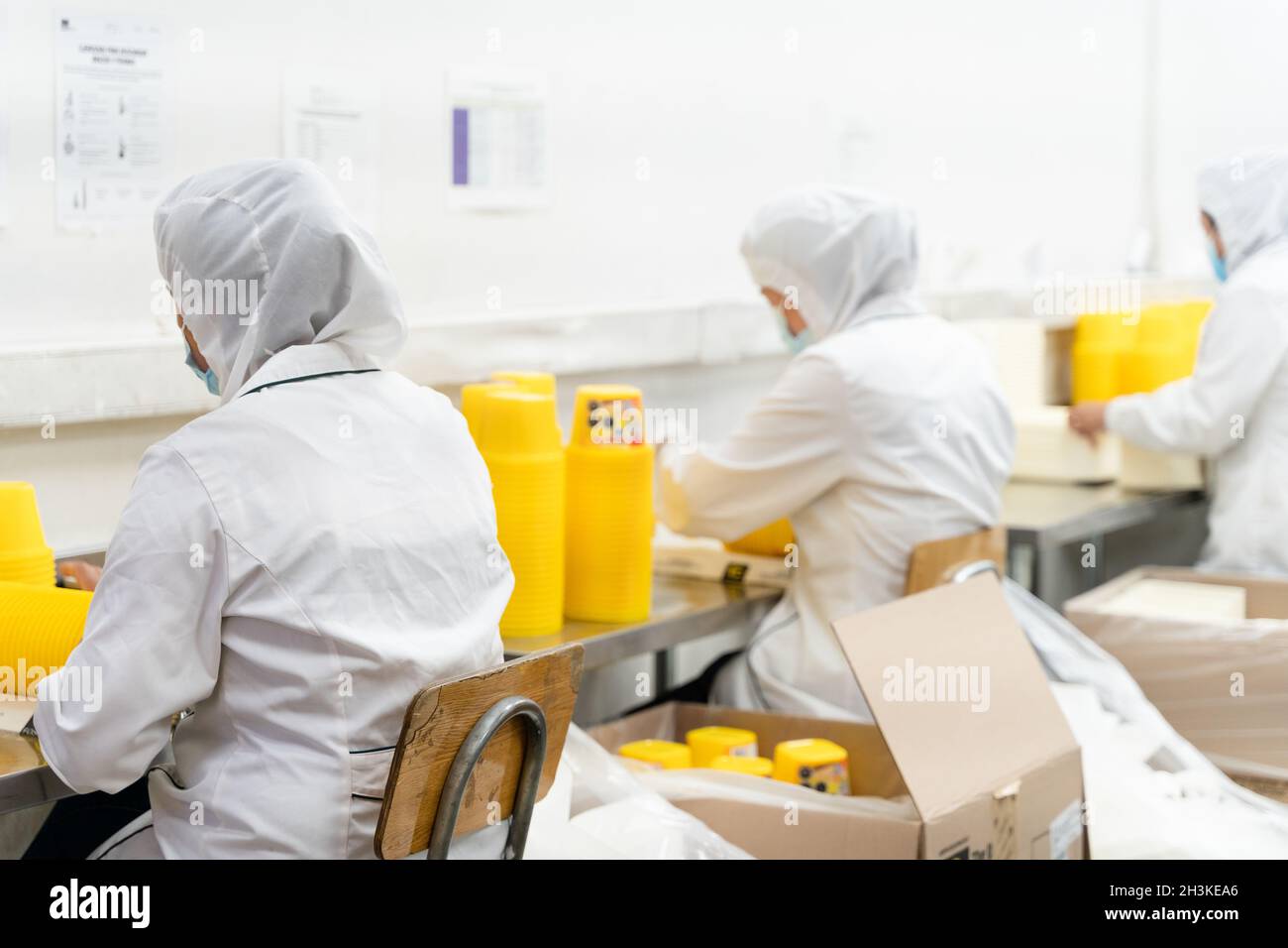 Anonyme Arbeiter auf weißen Schutzuniformen, die gelbe Behälter in der Industriefabrik verpacken. Produktionslinie, Qualitätskontrolle Arbeitskonzepte Stockfoto