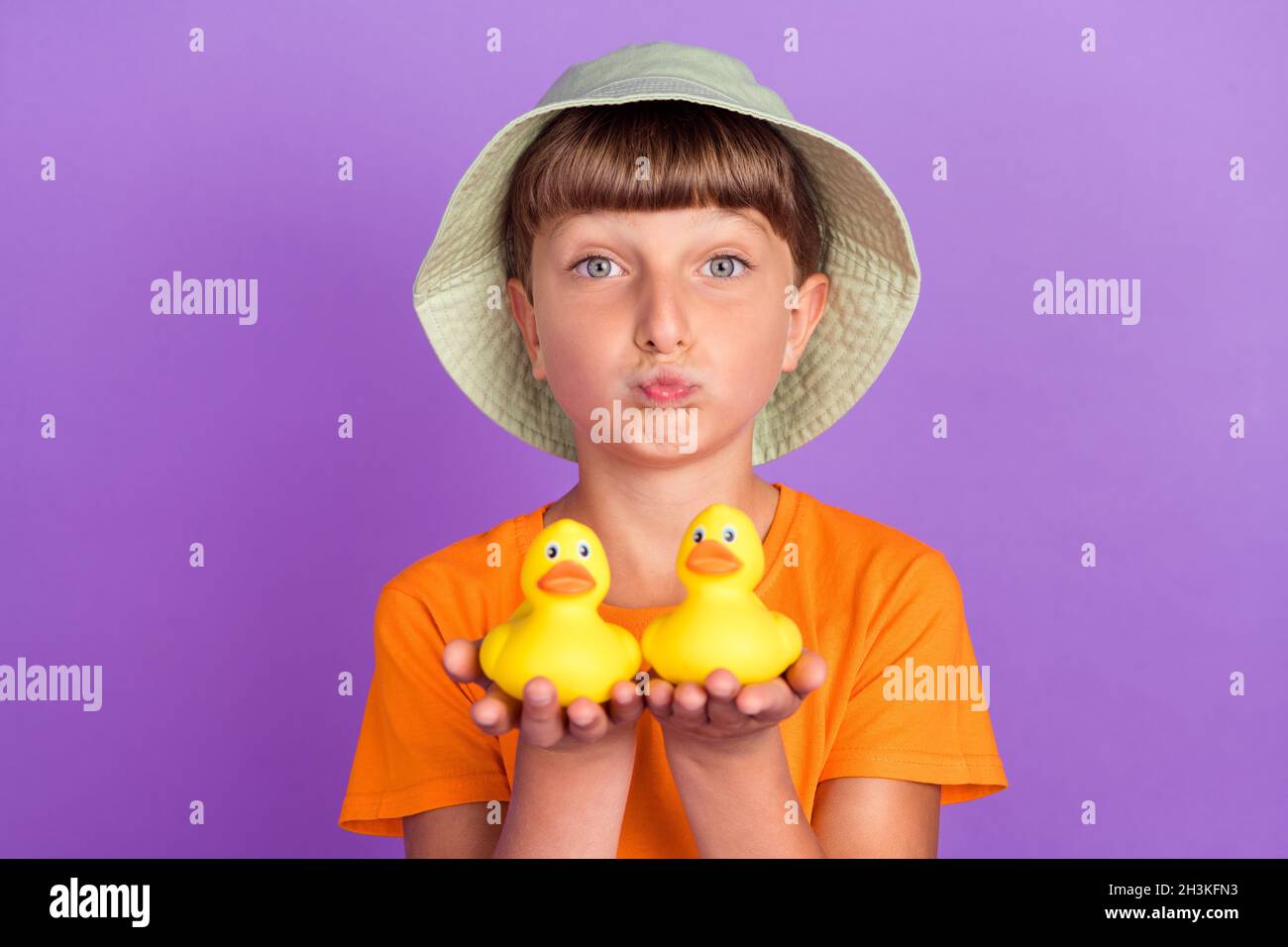Foto Porträt kleiner Junge trägt Kopfbedeckung senden Luftkuss halten Gummienten isoliert pastellvioletten Hintergrund Stockfoto