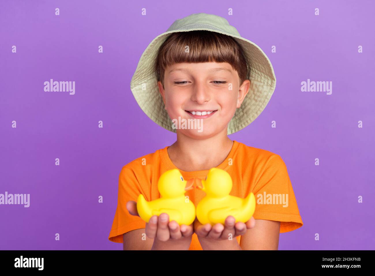 Foto Porträt kleiner Junge trägt Kopfbedeckung halten Gummienten lächeln isoliert pastelllila Farbe Hintergrund Stockfoto