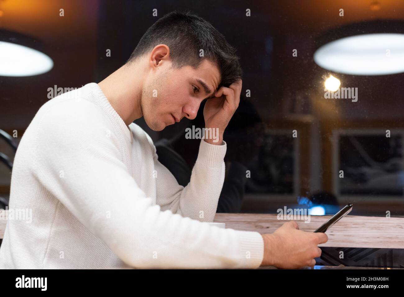 Frustrierter kaukasischer junger Mann, der Nachrichten mit enttäuschenden Nachrichten auf dem digitalen Smartphone liest. Stockfoto