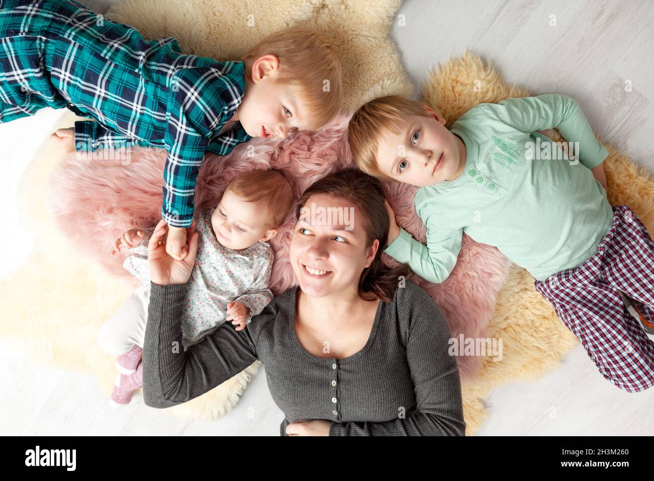 Draufsicht auf die schöne junge Mutter, ihre niedliche kleine Tochter und zwei Sohn, die auf Holzboden liegen. Stockfoto