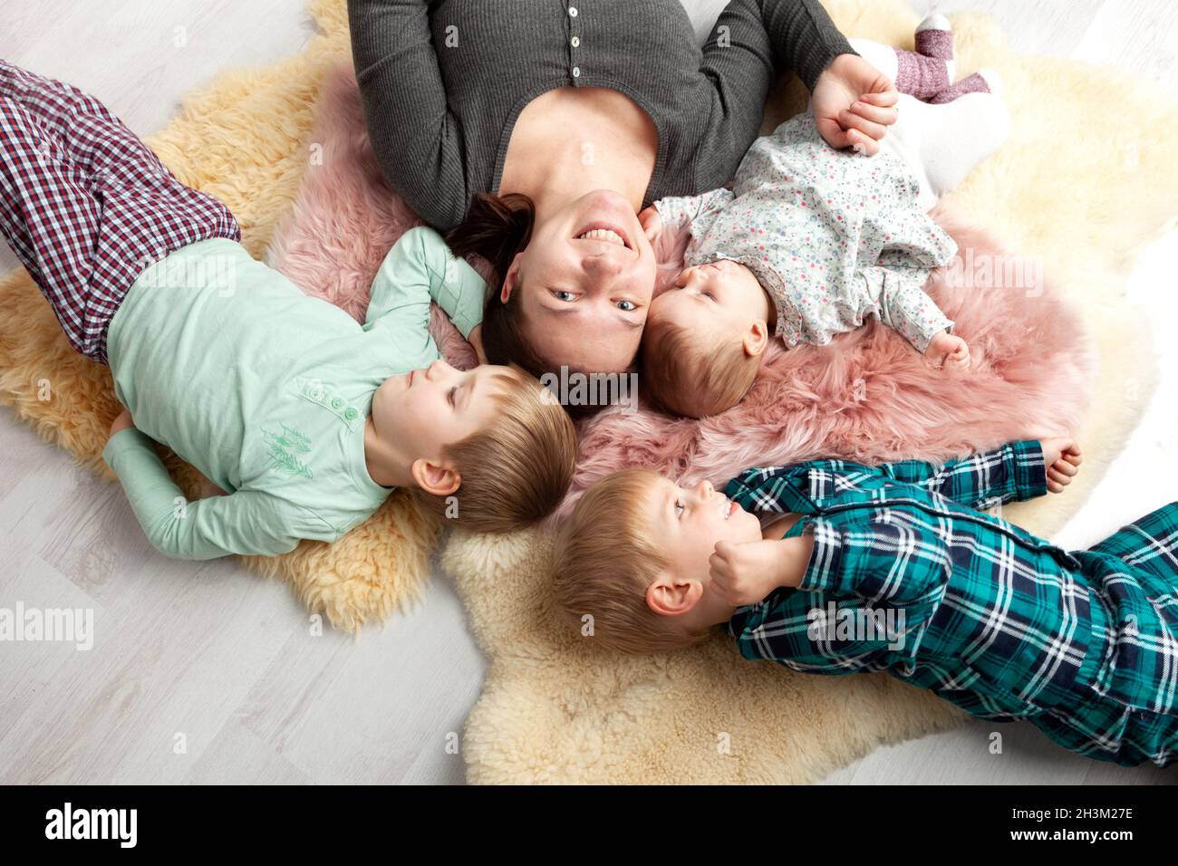 Draufsicht auf die schöne junge Mutter, ihre niedliche kleine Tochter und zwei Sohn, die auf Holzboden liegen. Stockfoto