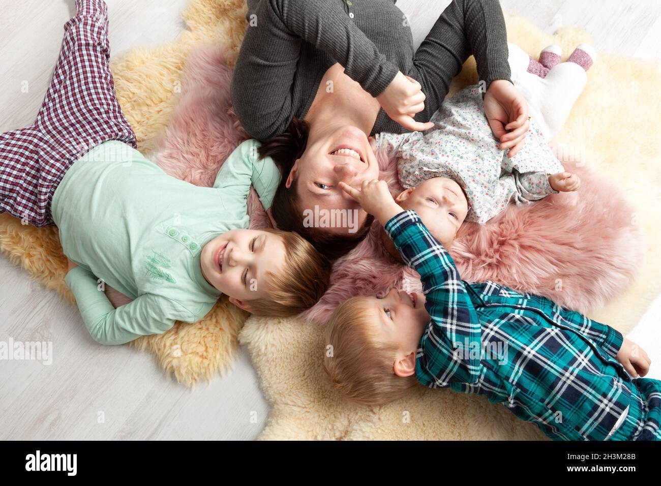 Draufsicht auf die schöne junge Mutter, ihre niedliche kleine Tochter und zwei Sohn, die auf Holzboden liegen. Stockfoto