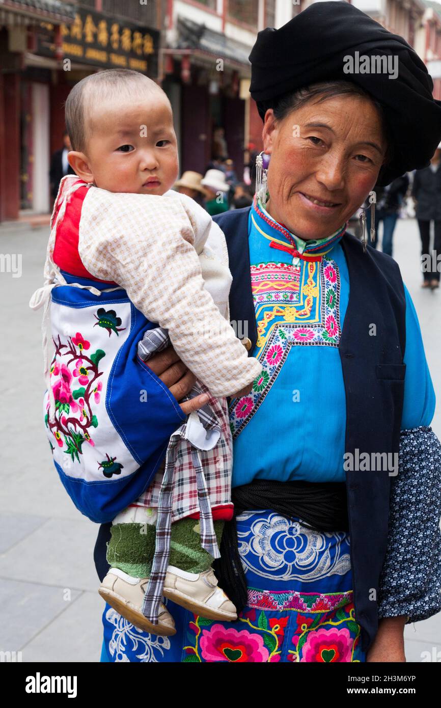 Frau in traditionellen tibetischen Kleidern mit Baby/Kleinkind, wahrscheinlich mit ihrem Enkelkind: Tibeterin/ethnische Frauen, wohnhaft oder ortsansässig in der alten chinesischen Stadt (alte ummauerte Stadt) von Songpan im Norden von Sichuan, China (125) Stockfoto