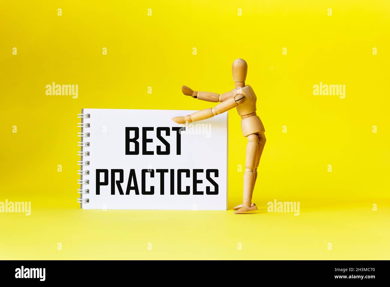 Best Practices: Der Text wird auf einem Notizbuch neben einer Holzpuppe auf einem gelben Hintergrund geschrieben. Positives Zitat. Stockfoto