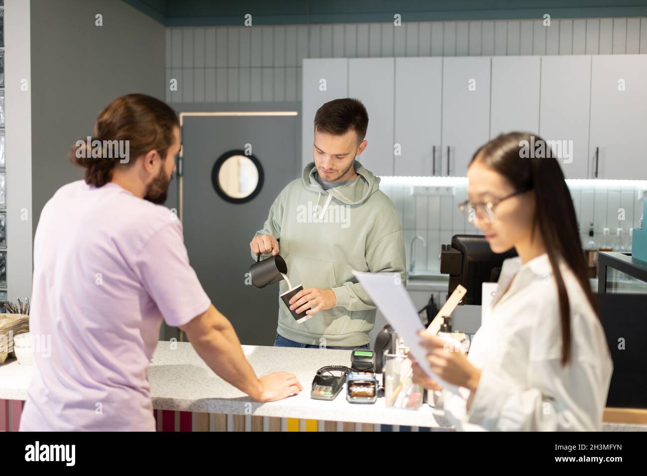 Der Barista gießt Milch in die Tasse, während er Kaffee für Gäste in der Schlange zubereitet Stockfoto