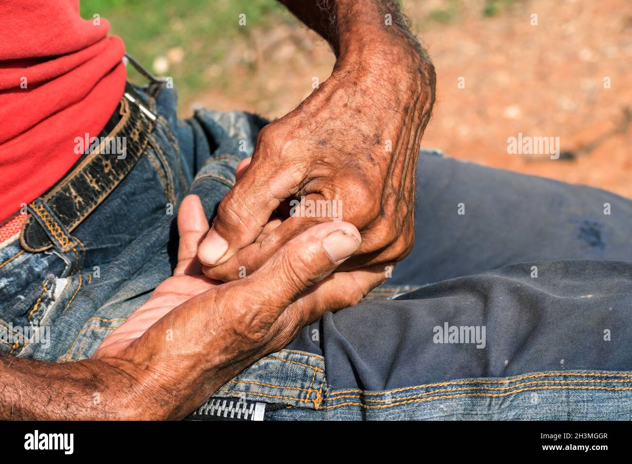 Nahaufnahme beider Hände eines älteren Mannes mit dunkler Haut, eine Hand befindet sich in der anderen, beide Hände auf seinem Schoß. Er hat eine kaltblütige Haut. Stockfoto