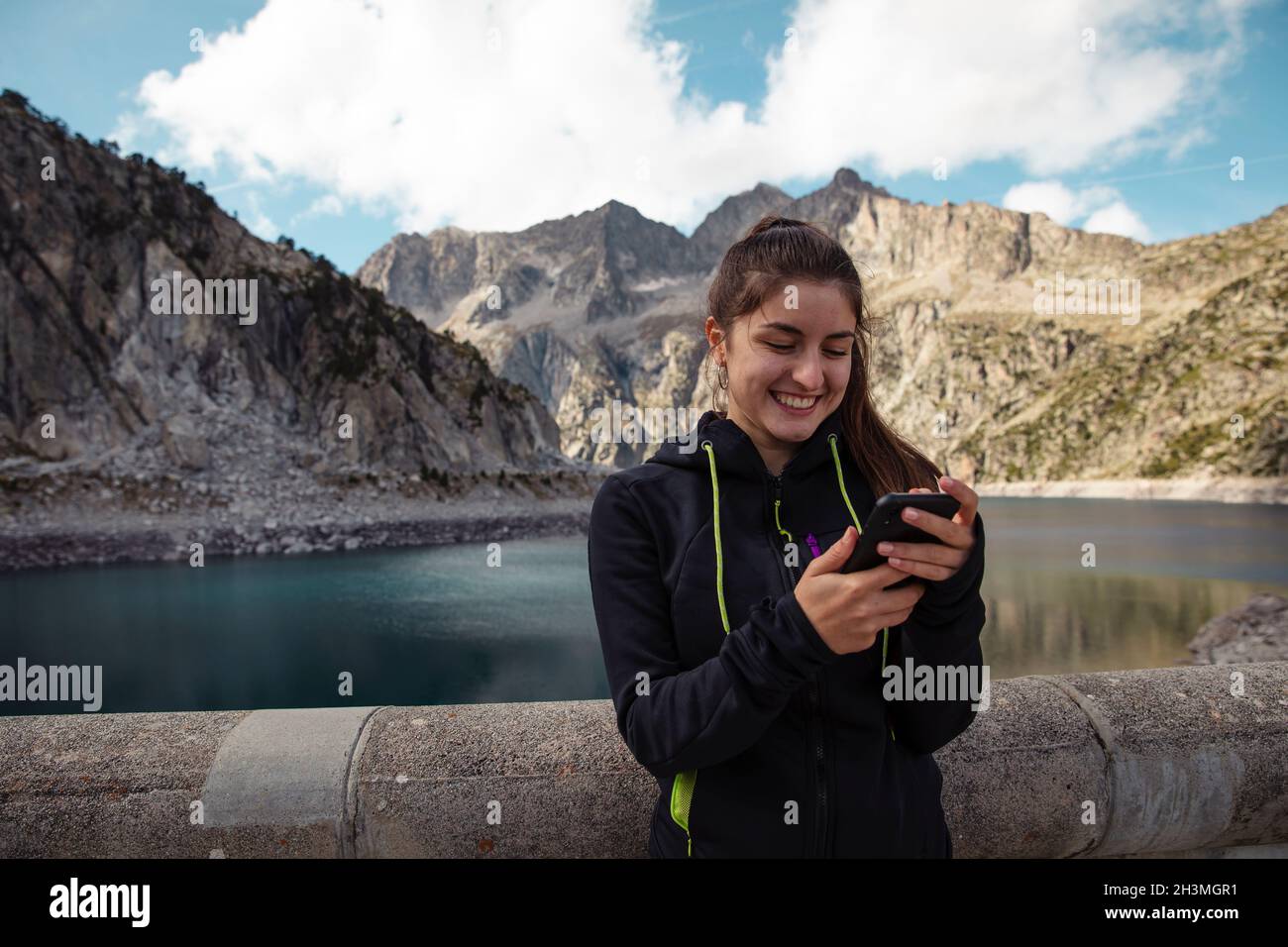 Mädchen, die mit dem Handy mit einem See im Hintergrund typisieren Stockfoto