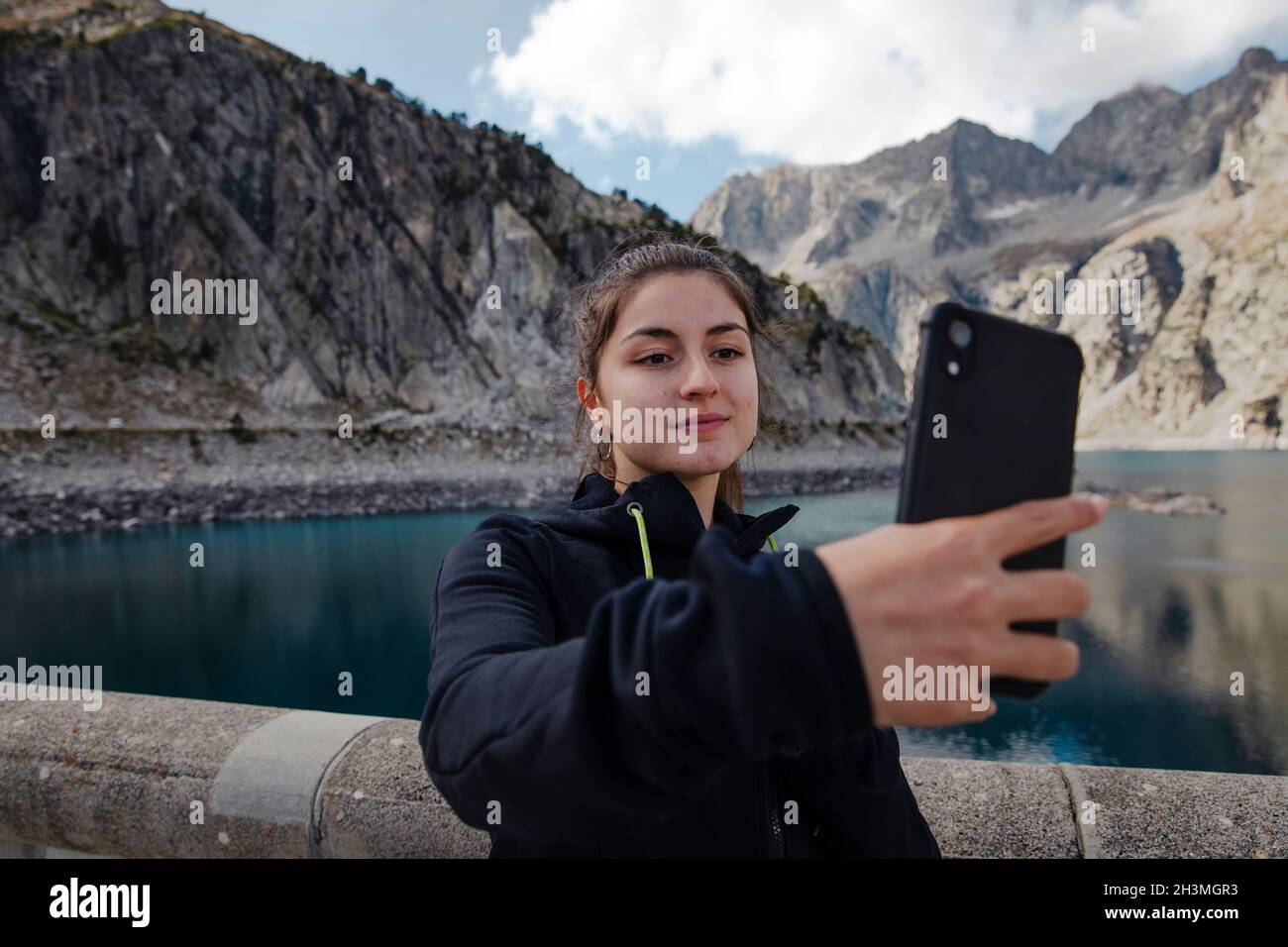 Mädchen nimmt ein Selfie mit dem Handy mit einem See im Hintergrund Stockfoto