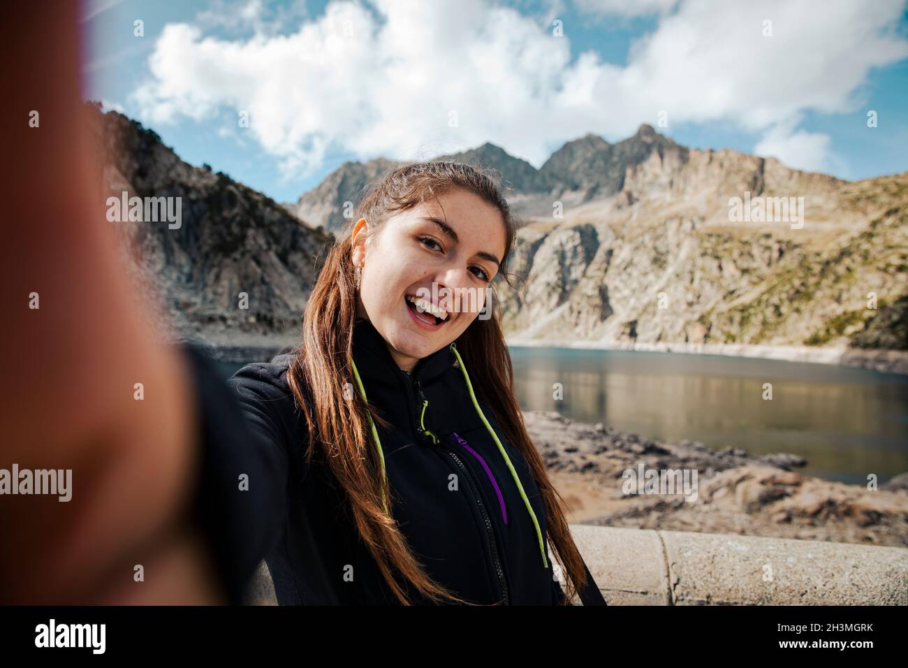 Mädchen nimmt ein Selfie, während sie lächelt mit einem See im Hintergrund Stockfoto
