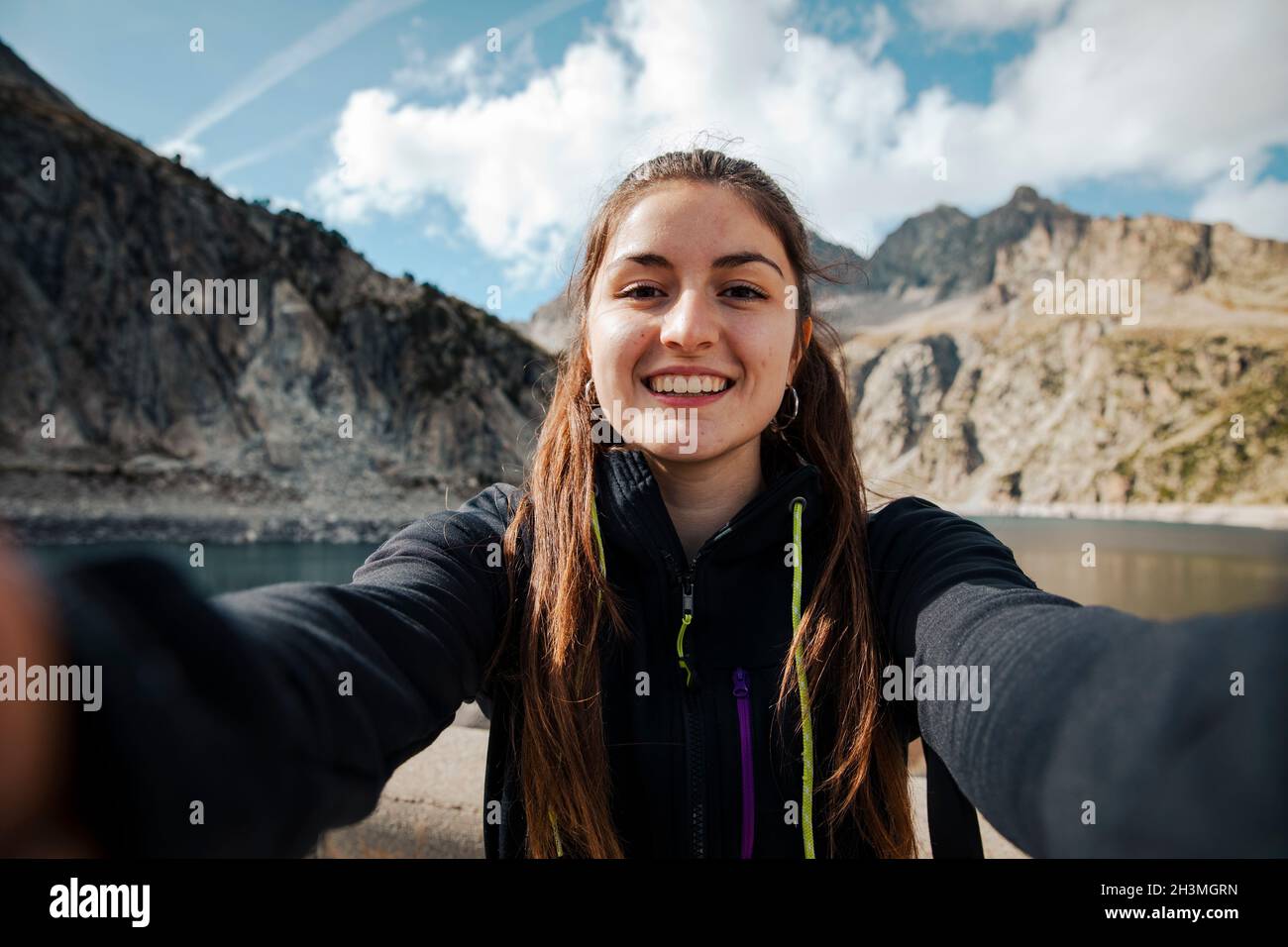 Mädchen nimmt ein Selfie, während sie lächelt mit einem See im Hintergrund Stockfoto