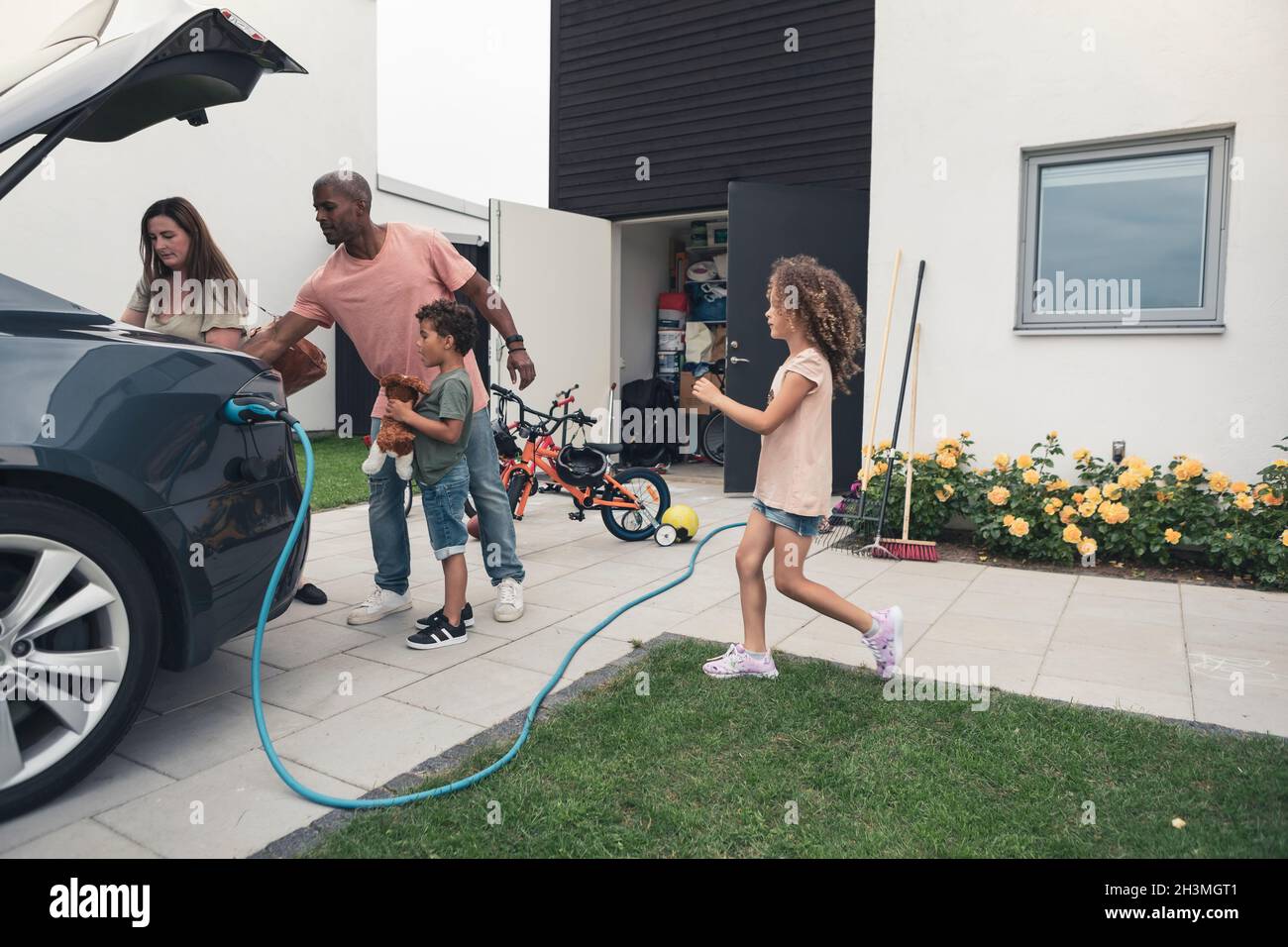 Familie lädt Gepäck im Kofferraum eines Elektroautos auf dem Vorhof Stockfoto