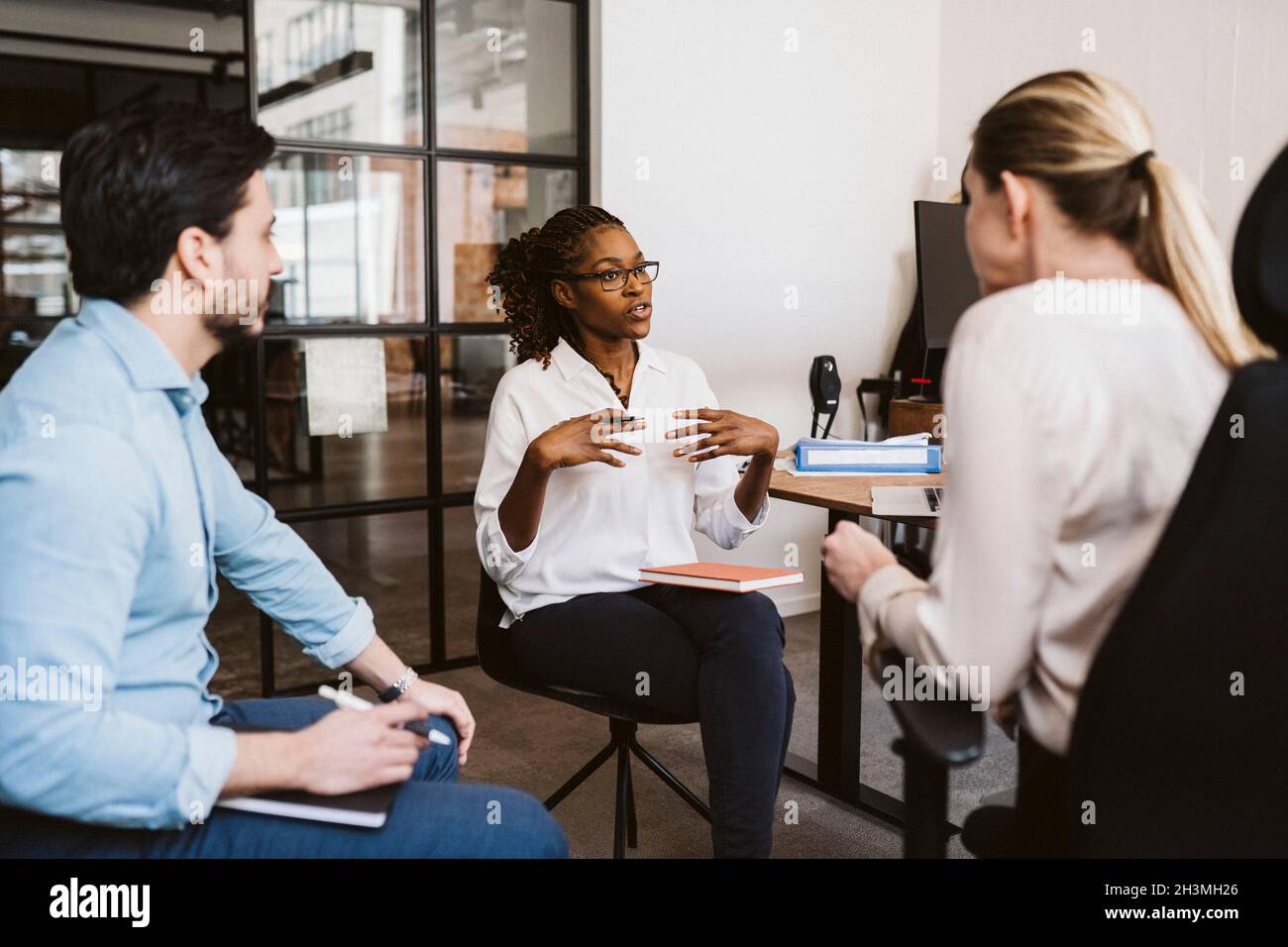 Eine Geschäftsfrau mit mittlerem Erwachsenenalter erklärt, während sie mit männlichen und weiblichen Kollegen im Kreativbüro diskutiert Stockfoto