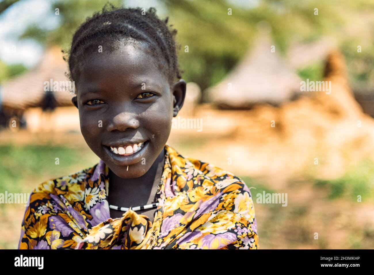 BOYA-STAMM, SÜDSUDAN - 10. MÄRZ 2020: Mädchen in traditionellem farbenfrohem Outfit und Accessoire lächelt vor der Kamera gegen verschwommenes SE Stockfoto