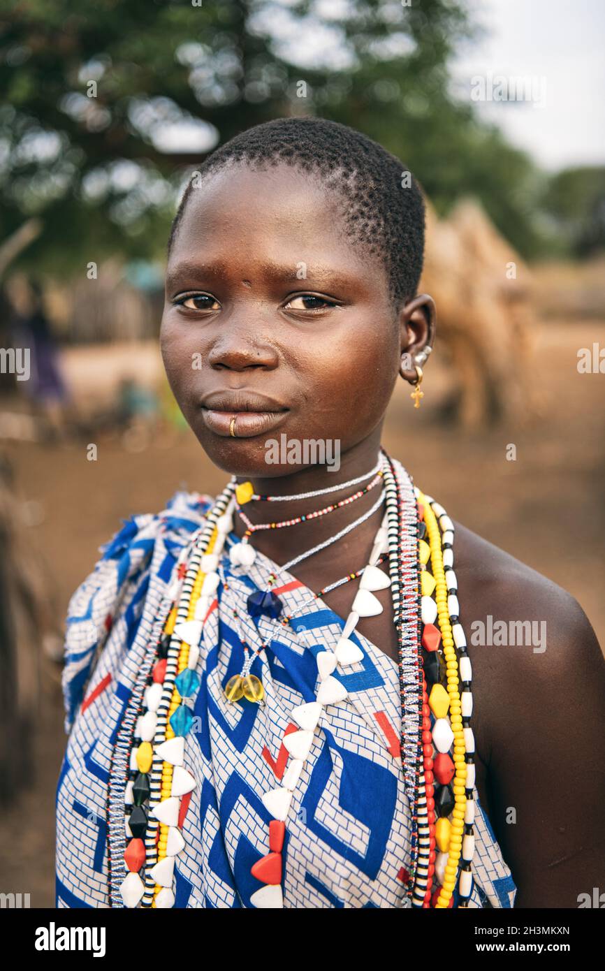 TOPOSA TRIBE, SÜDSUDAN - 12. MÄRZ 2020: Jugendliches Mädchen in ornamentalem Gewand und mit farbenfrohen Accessoires, die Kamera auf b betrachten Stockfoto