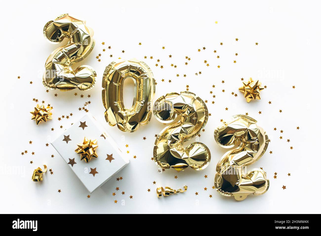 Luftballons aus Goldfolie mit den Zahlen 2022 und Geschenkbox auf weißem Hintergrund mit goldenen Pailletten. Weihnachten, Neujahr und Urlaubskonzept feiern. Flach liegend, Draufsicht. Stockfoto