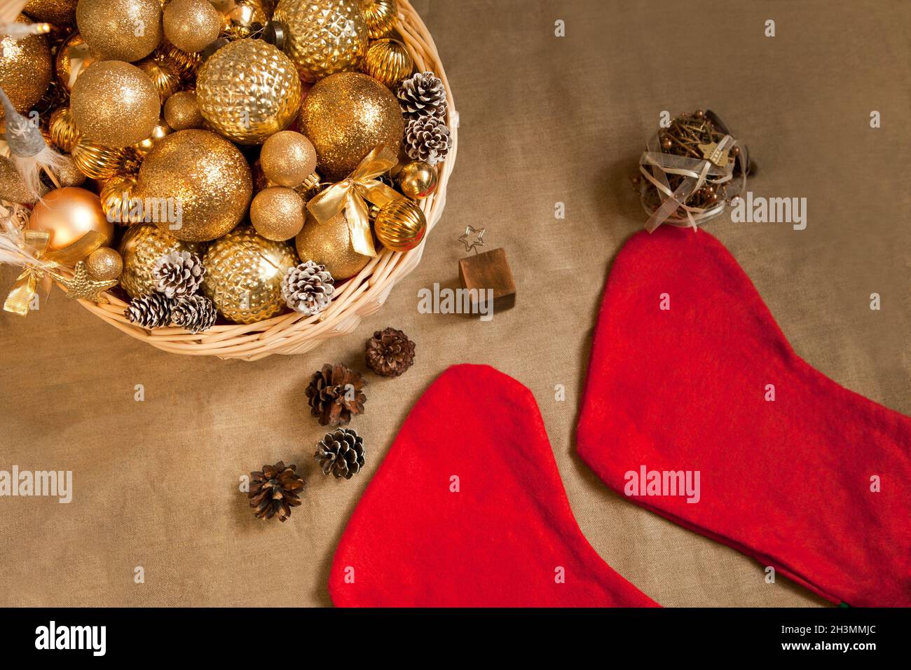 Riesiger Korbkorb gefüllt mit goldenen Bällen und Weihnachts-Weihnachtssocken auf Braun mit Tannenzapfen Stockfoto
