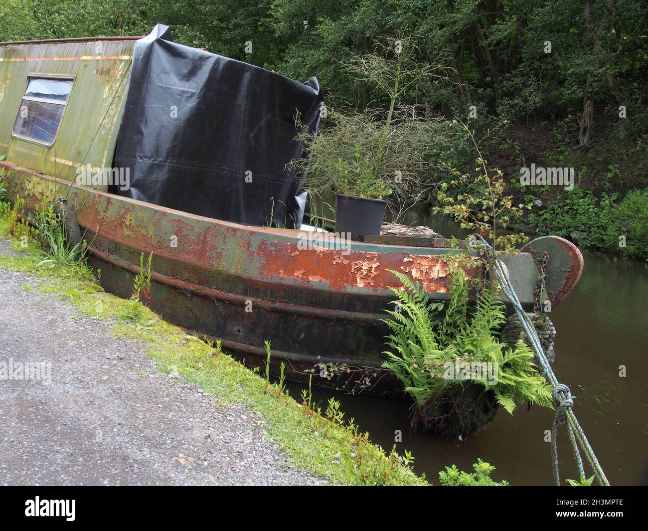 Ein altes rostendes Hausboot, das mit Unkraut überwuchert ist, vertäut am rochdale-Kanal, das zur Seite führt und zu sinken beginnt Stockfoto