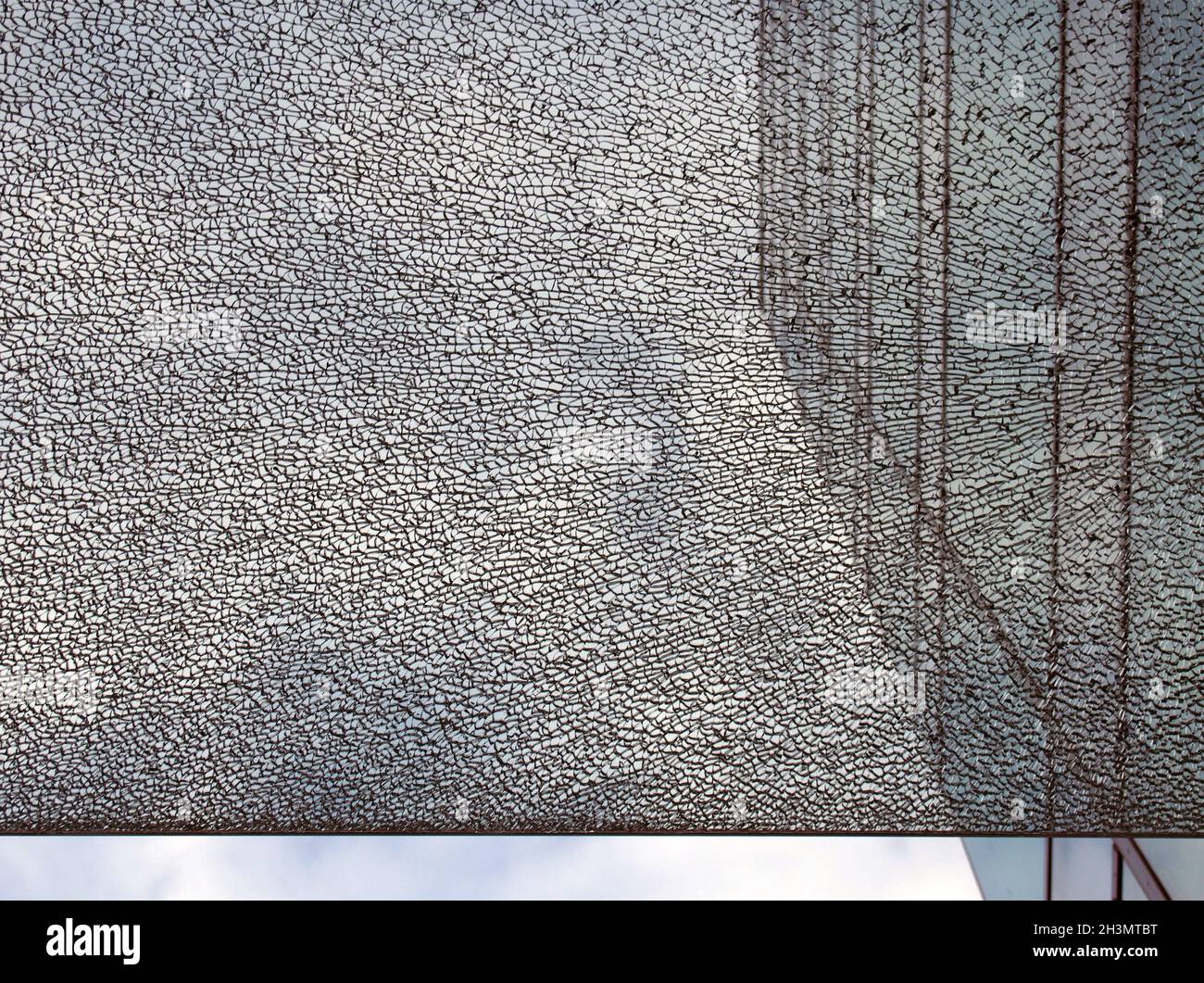 Eine Glasscheibe vor einem modernen Bürogebäude mit gerader Kante, die das Bild vor einem blau bewölkten Himmel teilt Stockfoto