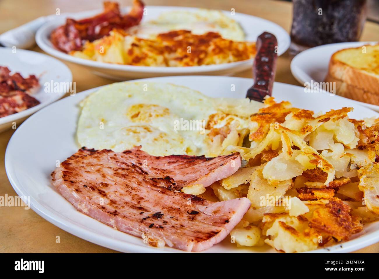 Frühstückstisch mit Schwerpunkt auf Schinken, Kartoffeln und Eiern Stockfoto