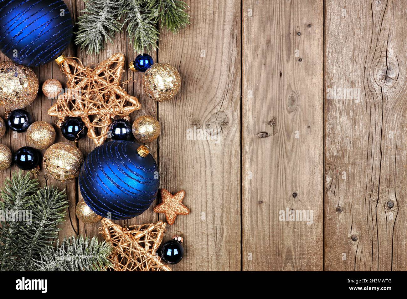 Weihnachtliche Seitenumrandung mit dunkelblauen und goldenen Ornamenten und Ästen. Blick von oben auf einem rustikalen Holzhintergrund. Stockfoto