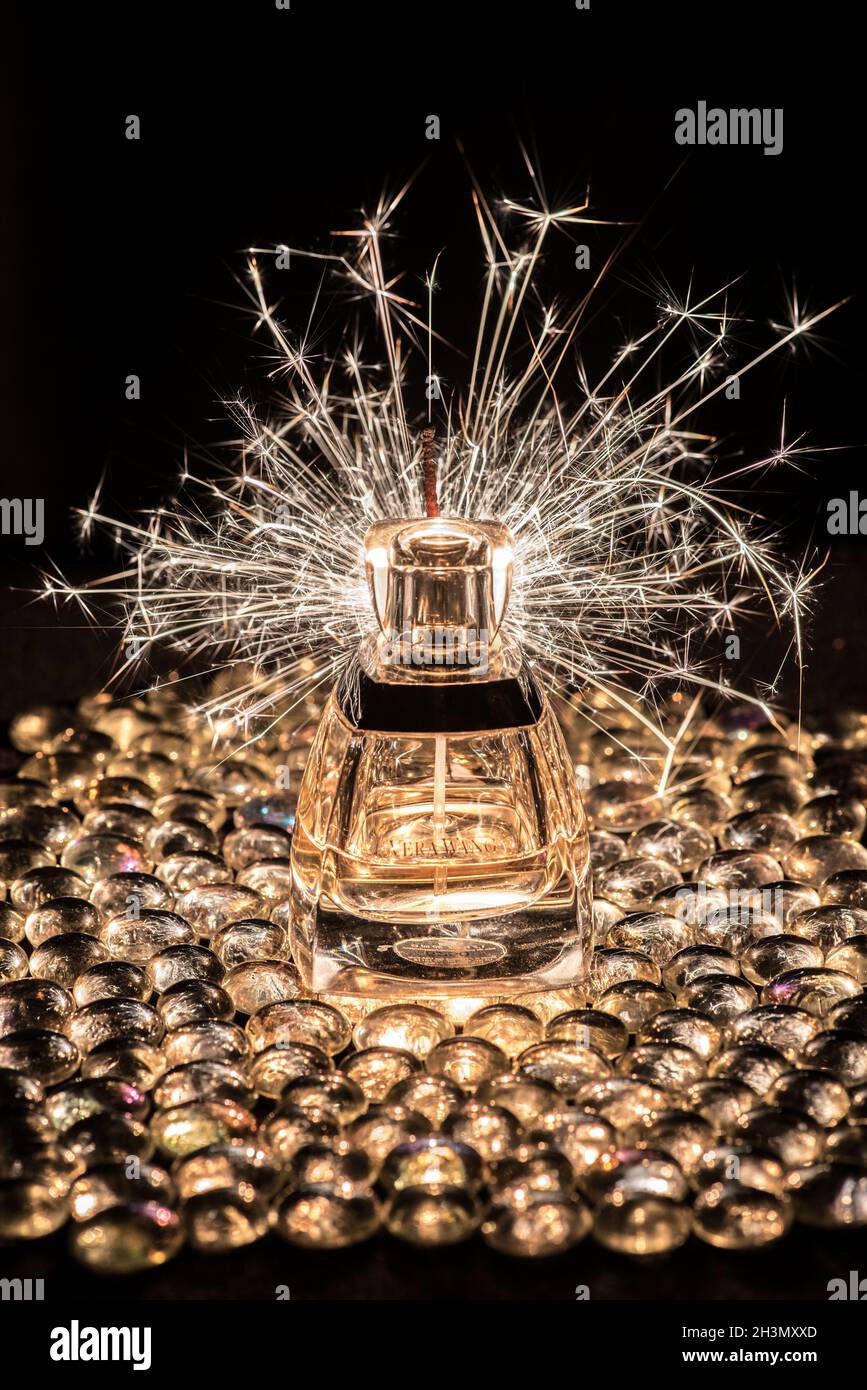 Ein brennender Funke wirft Funken über eine 'Vera Wang' Parfümflasche, die auf Glasperlen sitzt Stockfoto