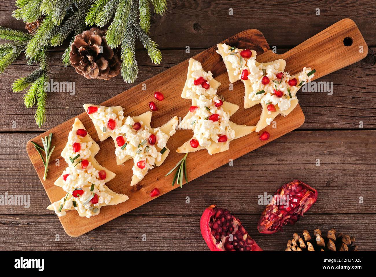 Weihnachtsbaum-Vorspeisen mit Feta-Käse, Granatapfel und Rosmarin. Ansicht von oben auf einem Servierbrett gegen Holz. Stockfoto