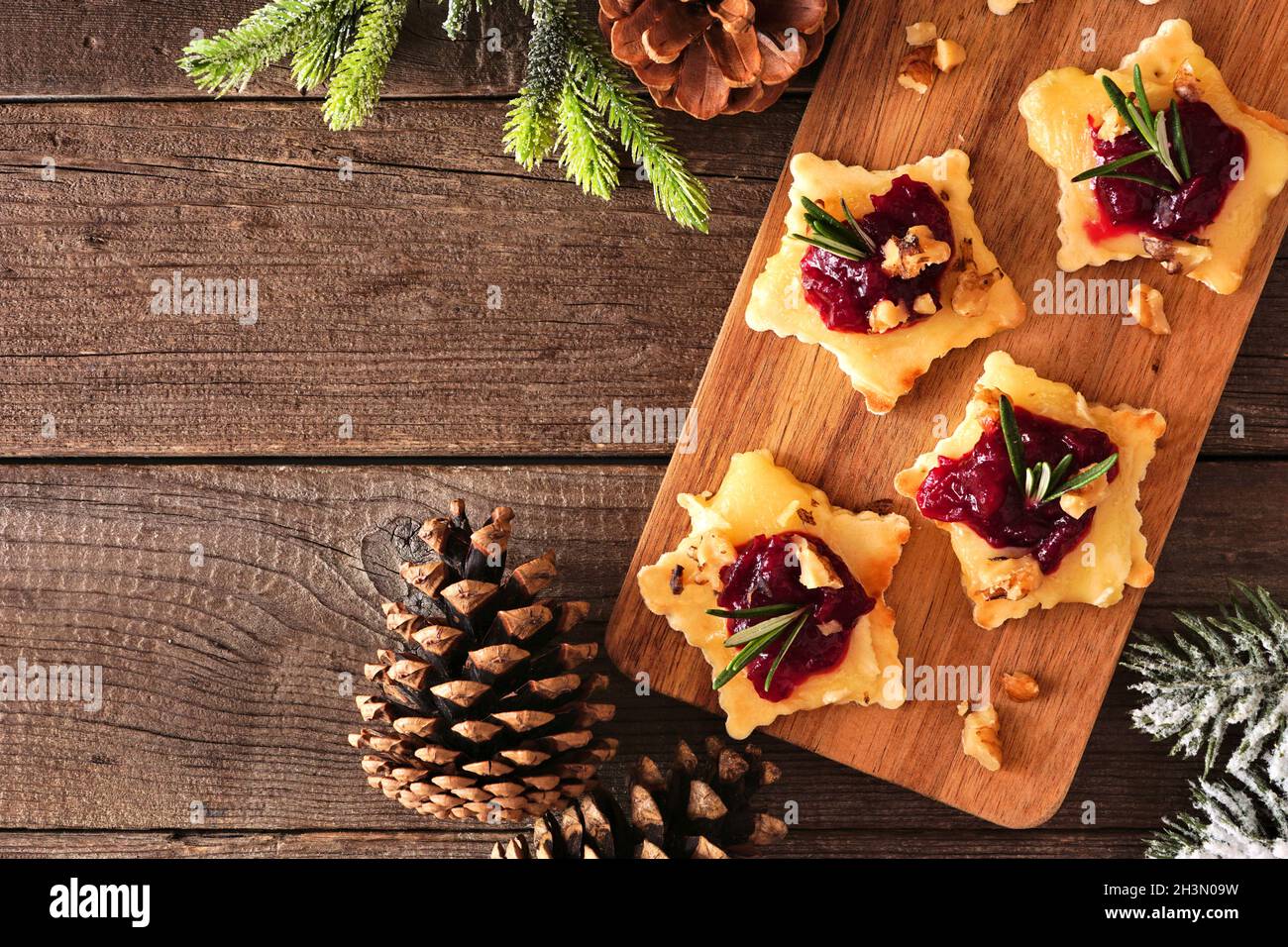 Weihnachtliche sternförmige Vorspeisen mit Preiselbeeren und gebratener Brie. Draufsicht auf einem Servierbrett vor einem Holzhintergrund. Speicherplatz kopieren. Stockfoto