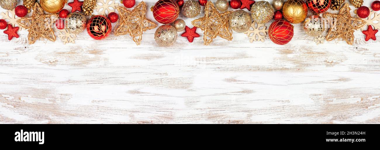 Weihnachtliche obere Bordüre aus roten und goldenen Ornamenten. Ansicht von oben auf einem weißen rustikalen weißen Holz Banner Hintergrund. Speicherplatz kopieren. Stockfoto
