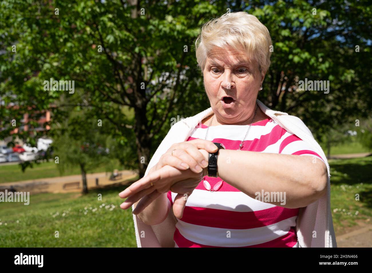 Ältere Frau, die den Park überraschenderweise anschaut. Ältere blonde Dame erkennt, dass sie an einem sonnigen Tag im Freien spät dran ist Stockfoto