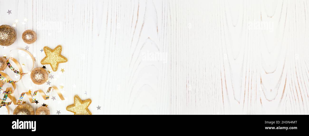 Silvester Eckbanner mit Konfetti, Luftschlangen und goldenen Verzierungen. Blick über einen weißen Holzhintergrund. Stockfoto