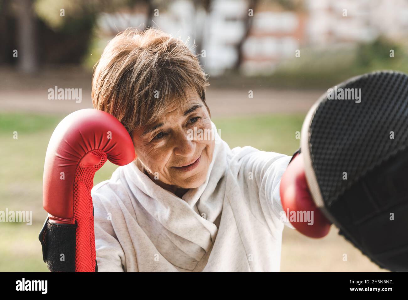 Ältere Frau, die im Stadtpark mit einem persönlichen Trainer ein Boxtraining macht - Fokus auf das Gesicht Stockfoto