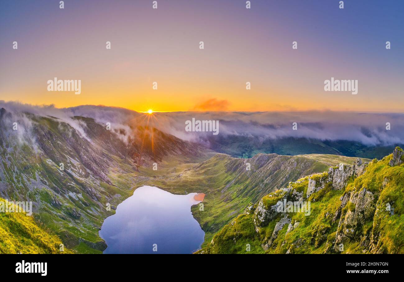Erstaunlicher Sonnenaufgang auf dem Cadair Idris Berg in Snowdonia, Nordwales. Die Sonne scheint auf dem Gletschersee, die herrliche Wolkeninversion, die Berge umhüllt. Stockfoto